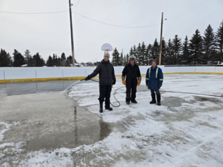 3 people filling ice rink with water from hose